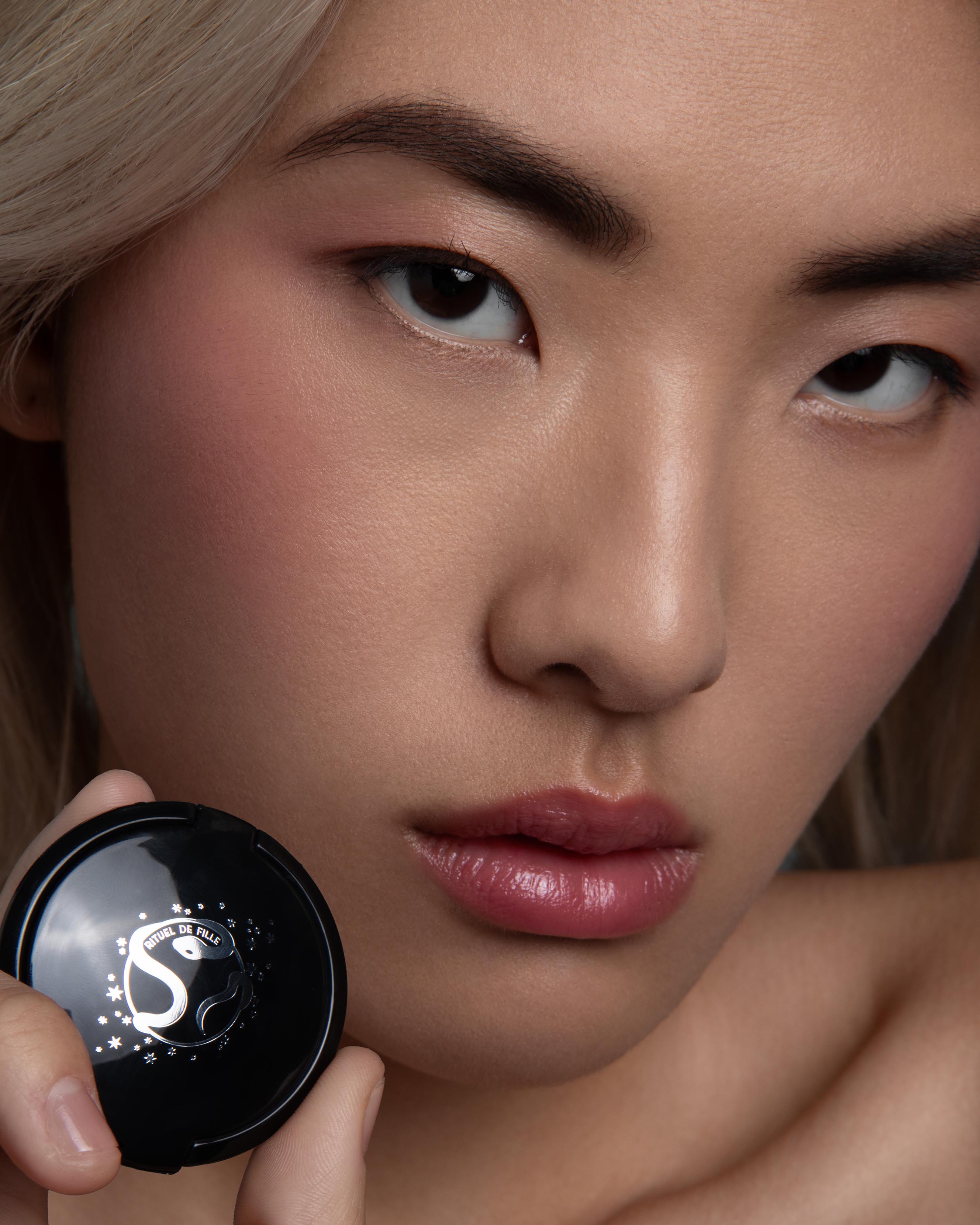 Close-up of a model holding a black compact with a Rituel de Fille logo.