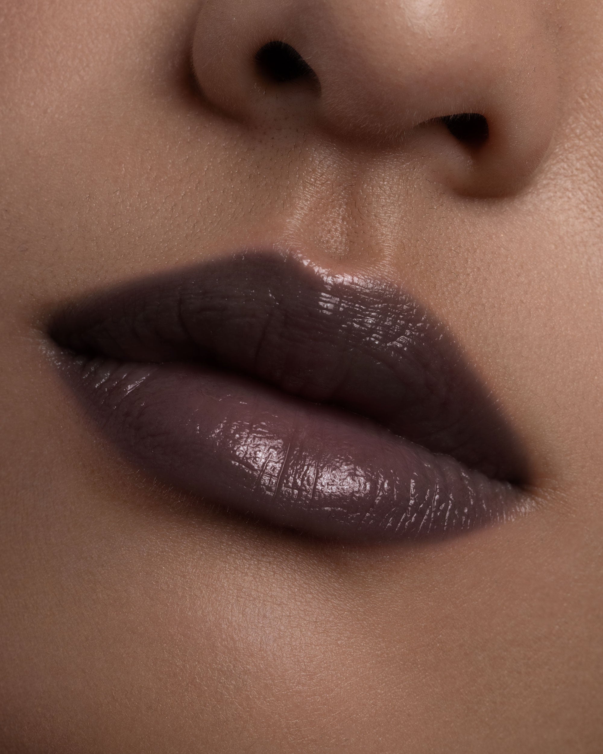 Close-up of a person's lips with a dark brown lipstick on a neutral background