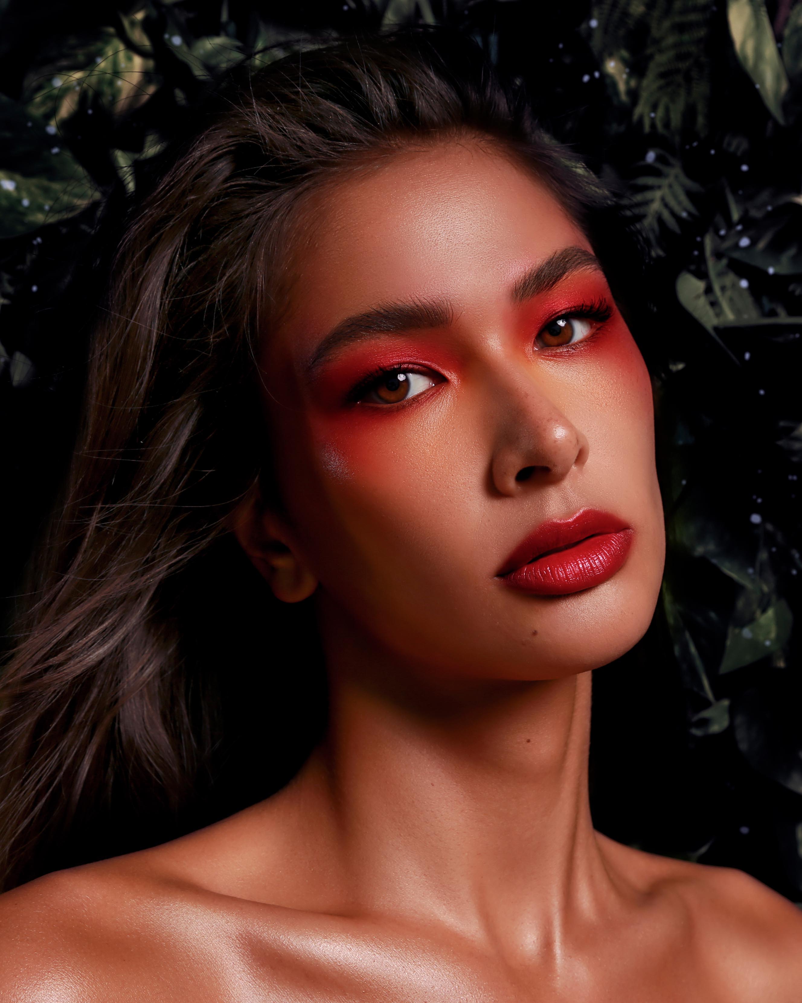 Close-up of a model with medium skin wearing red eye, lip, and cheek makeup
