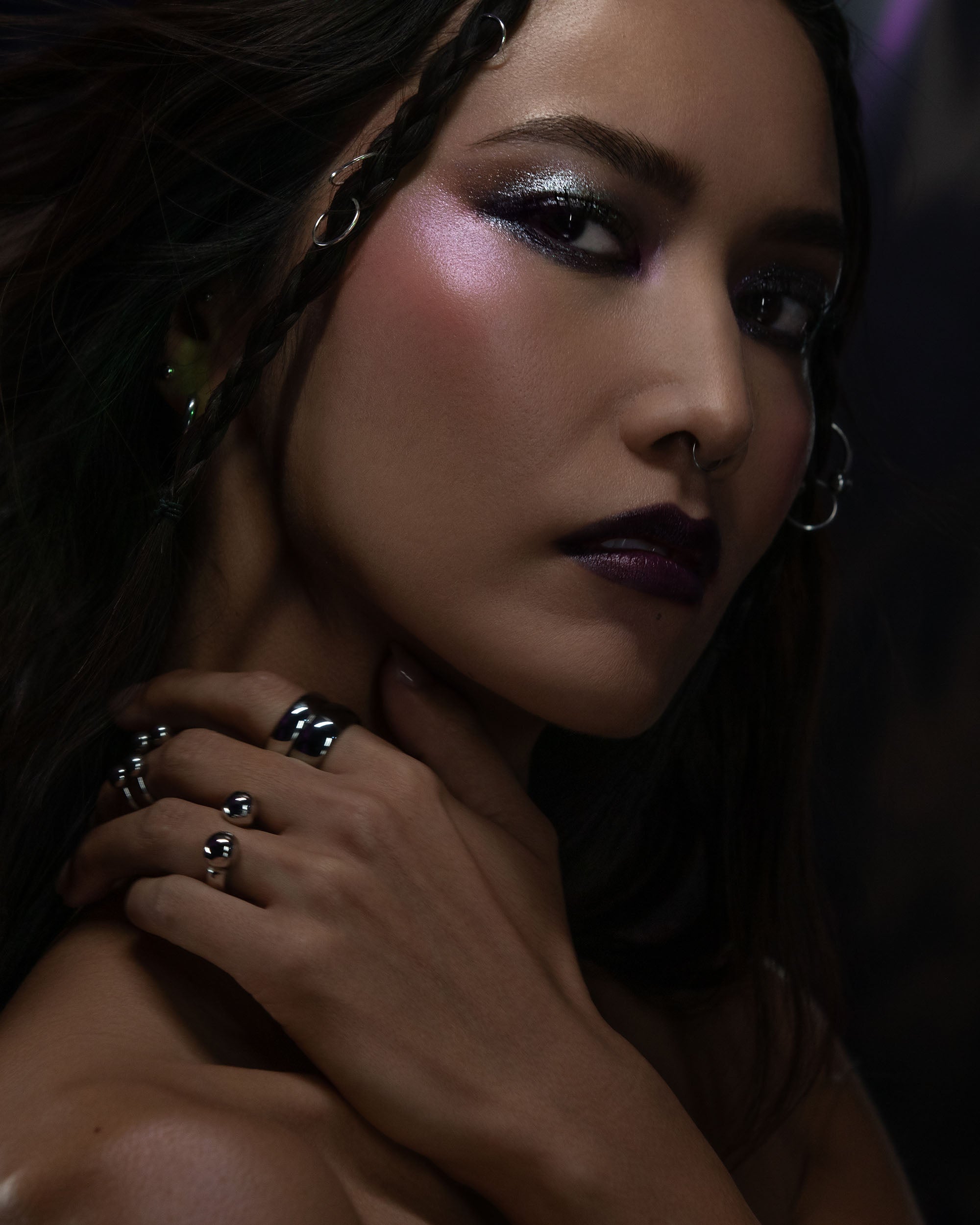 Close-up of a person with dark makeup and jewelry against a dark background