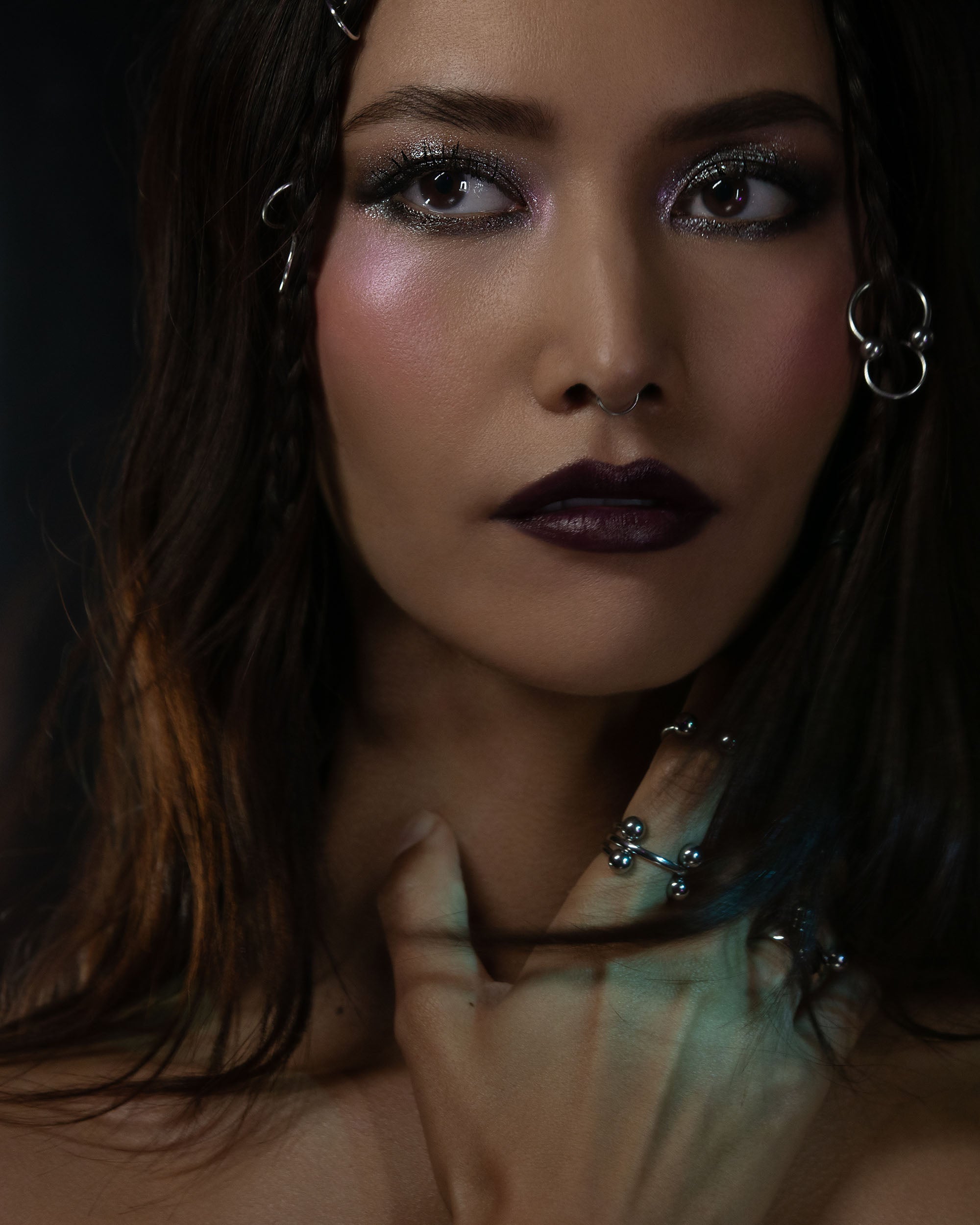 Close-up of a person with dark hair and makeup, wearing earrings.