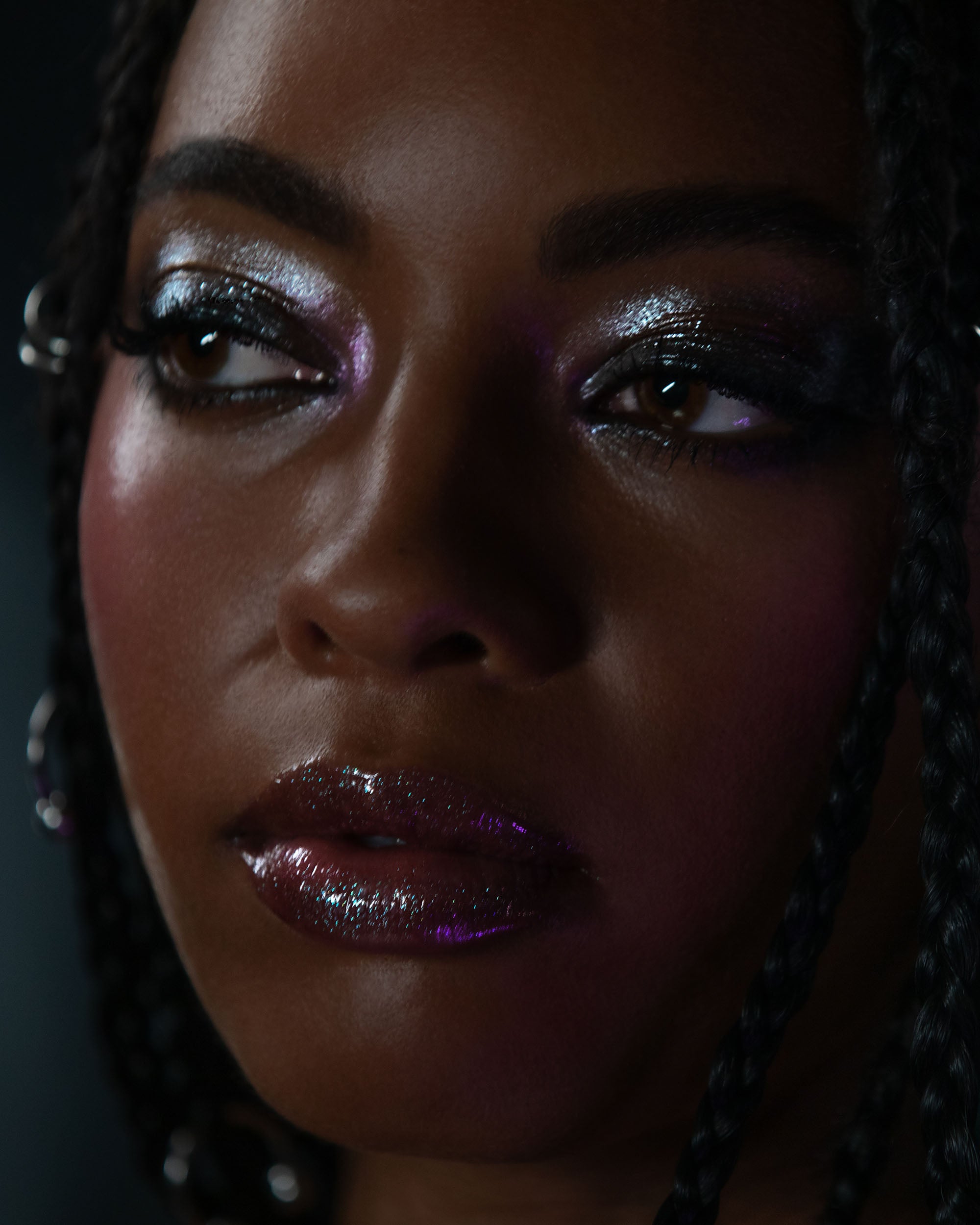 Close-up of a woman with glittery makeup and braided hair against a dark background