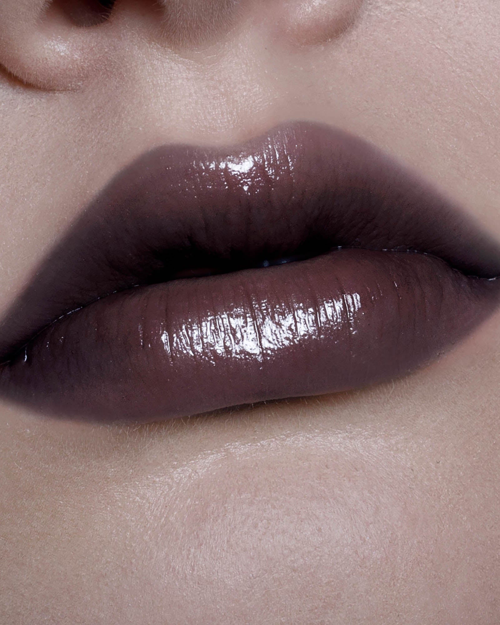 Close-up of a person's lips with a glossy brown lipstick.