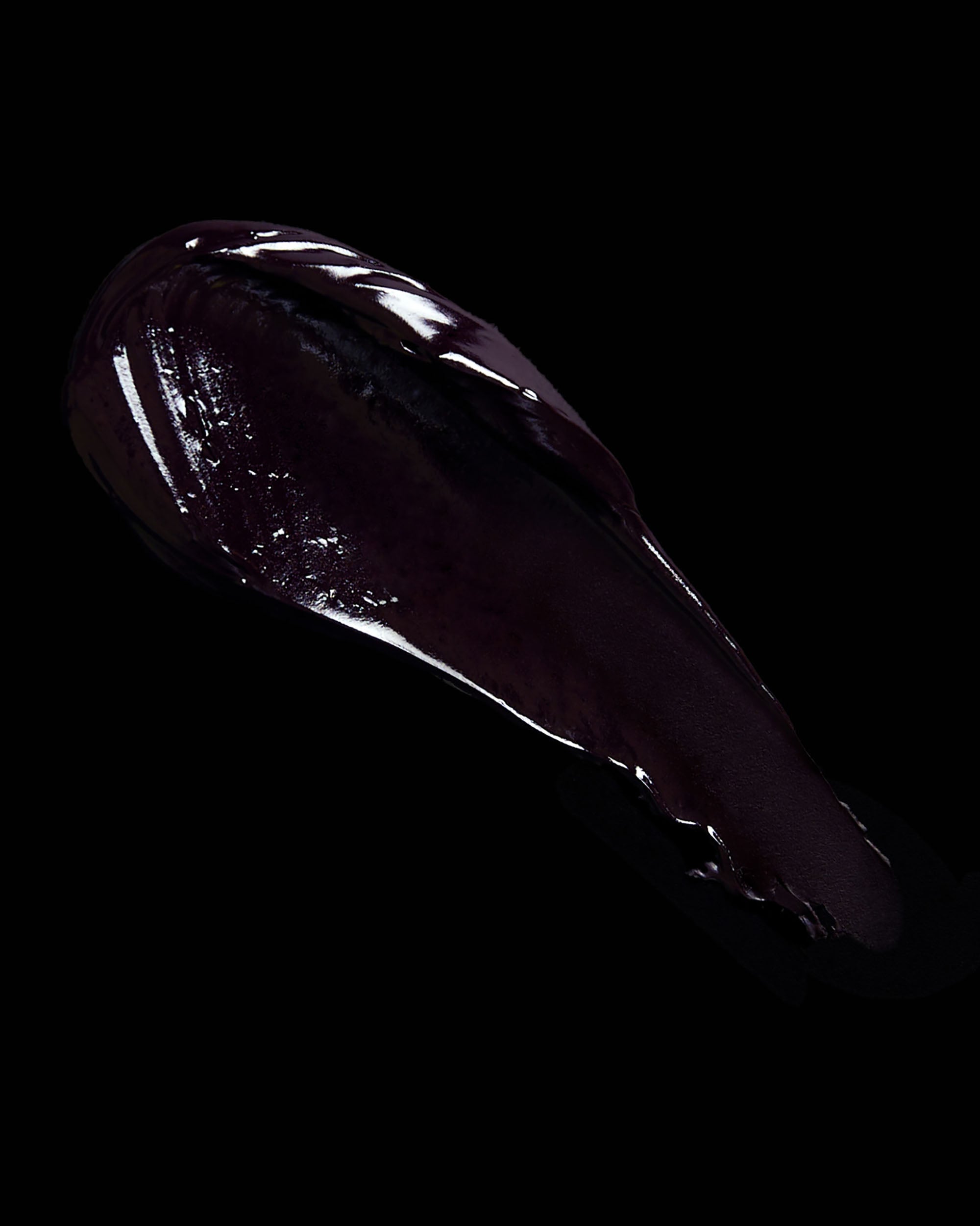 Glossy dark purple lipstick swatch on a black background