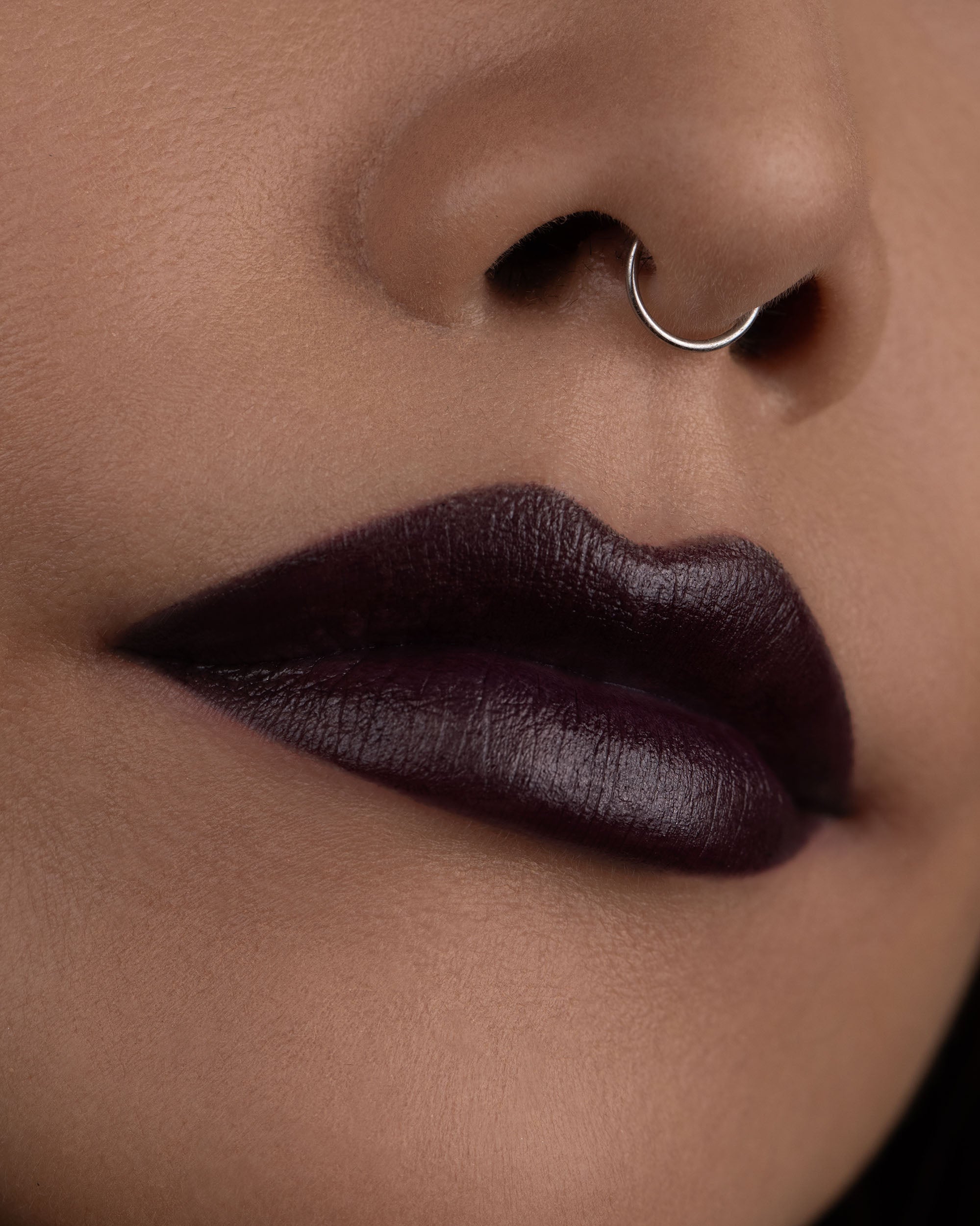 Close-up of a person's lips with dark lipstick and a nose ring.
