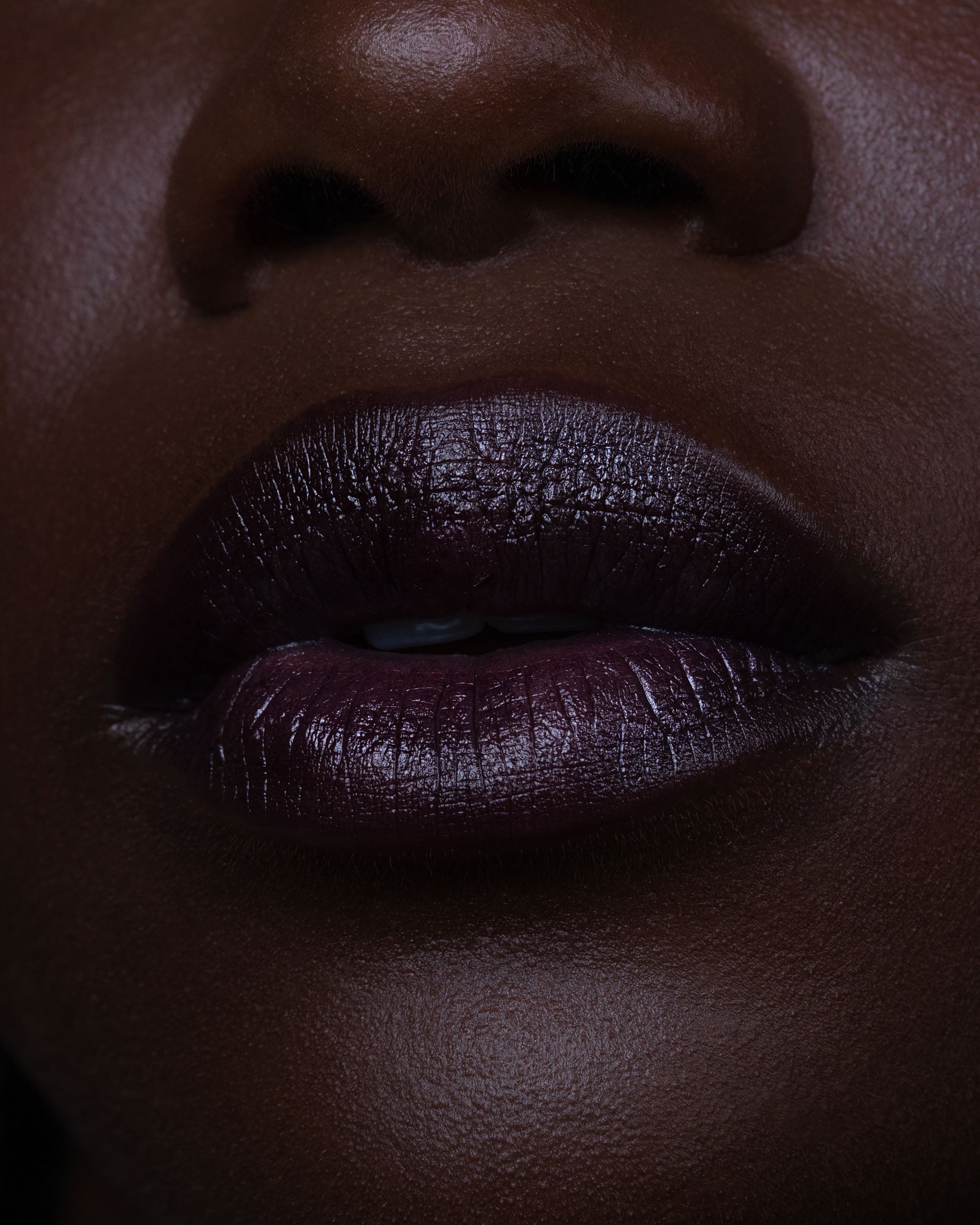 Close-up of a person's lips wearing dark purple lipstick on a deep skin tone.