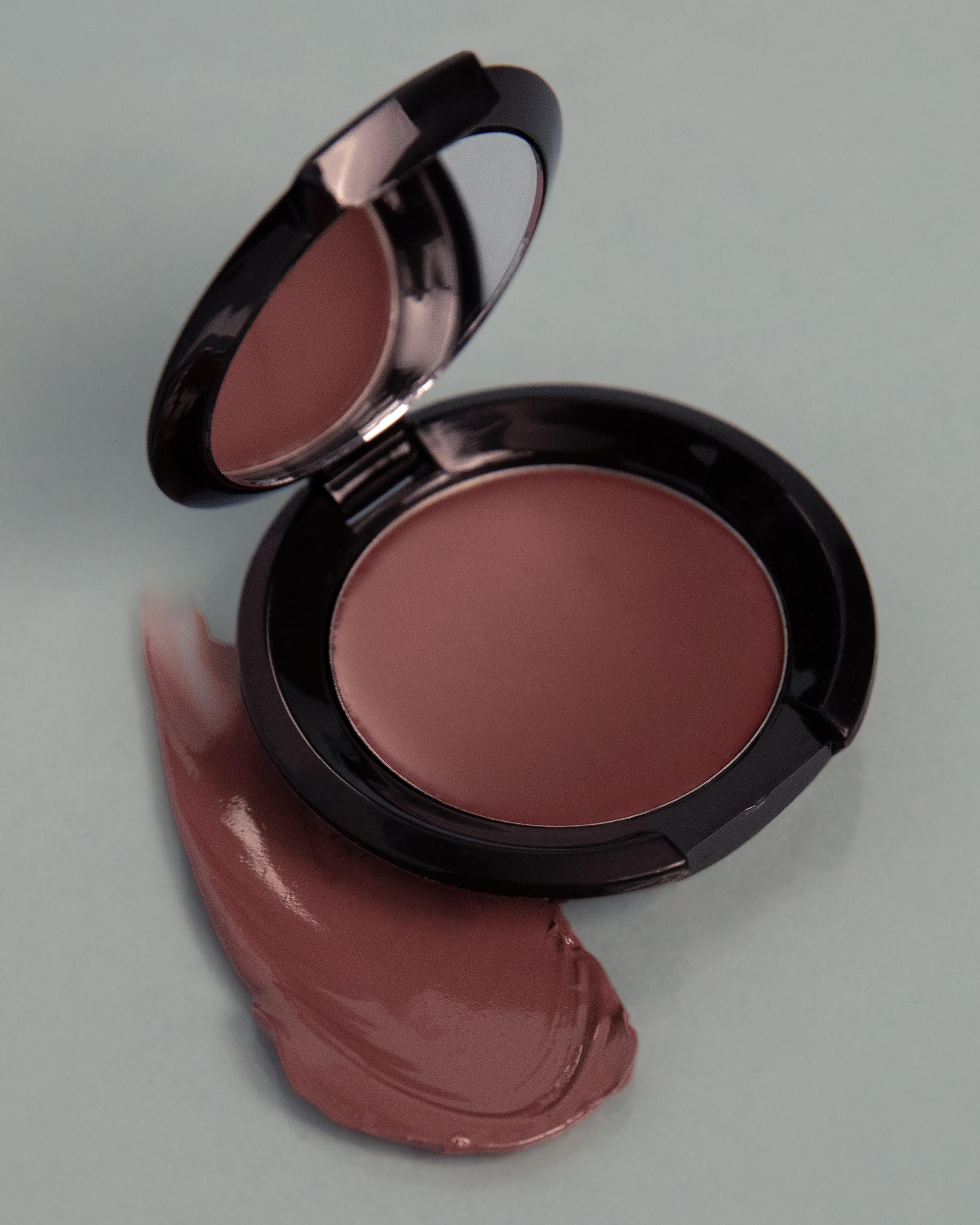 Open makeup compact with nude pink makeup on a light gray background