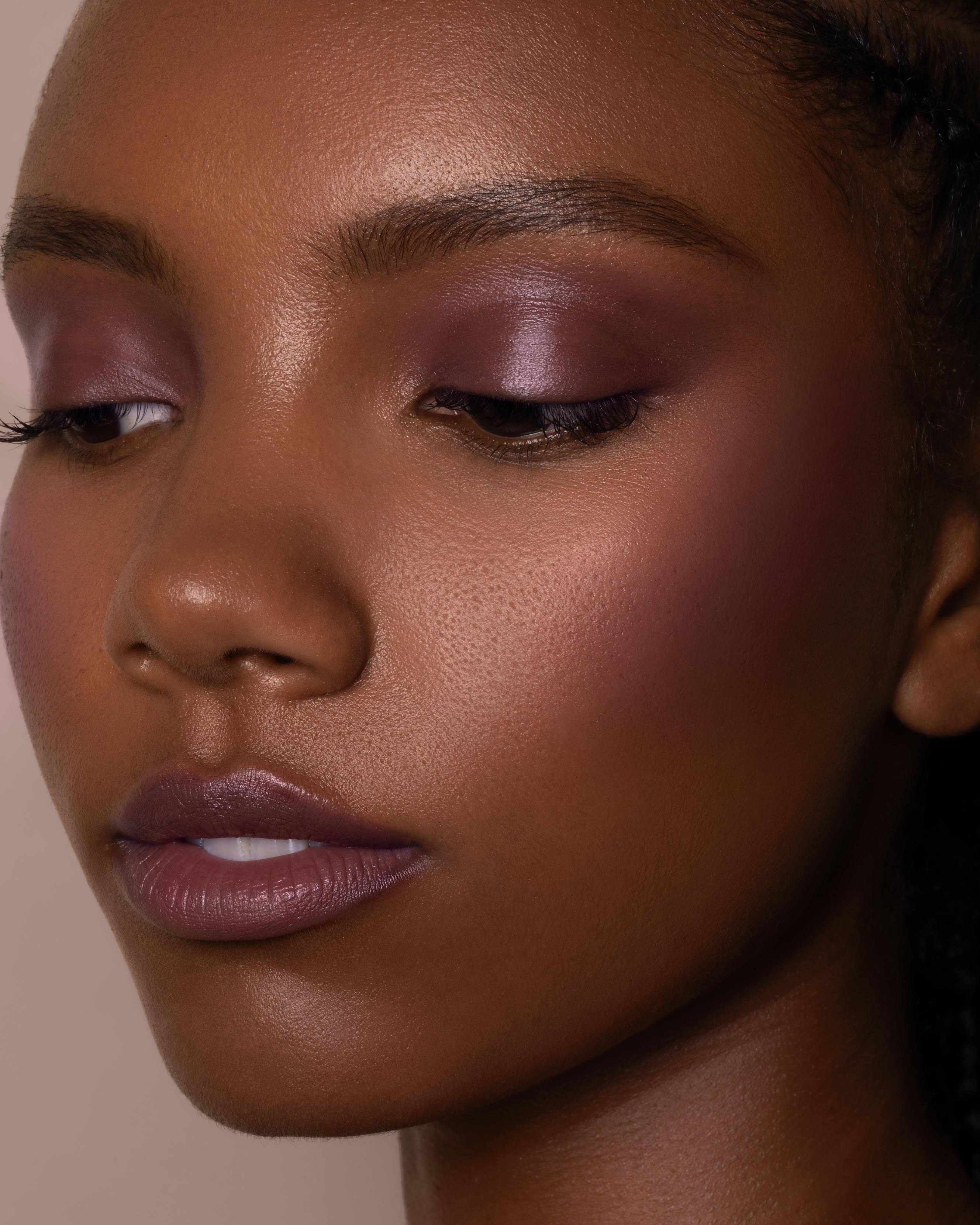 Close-up of a model with medium-deep skin wearing nude pink makeup on lips, eyes, and cheeks