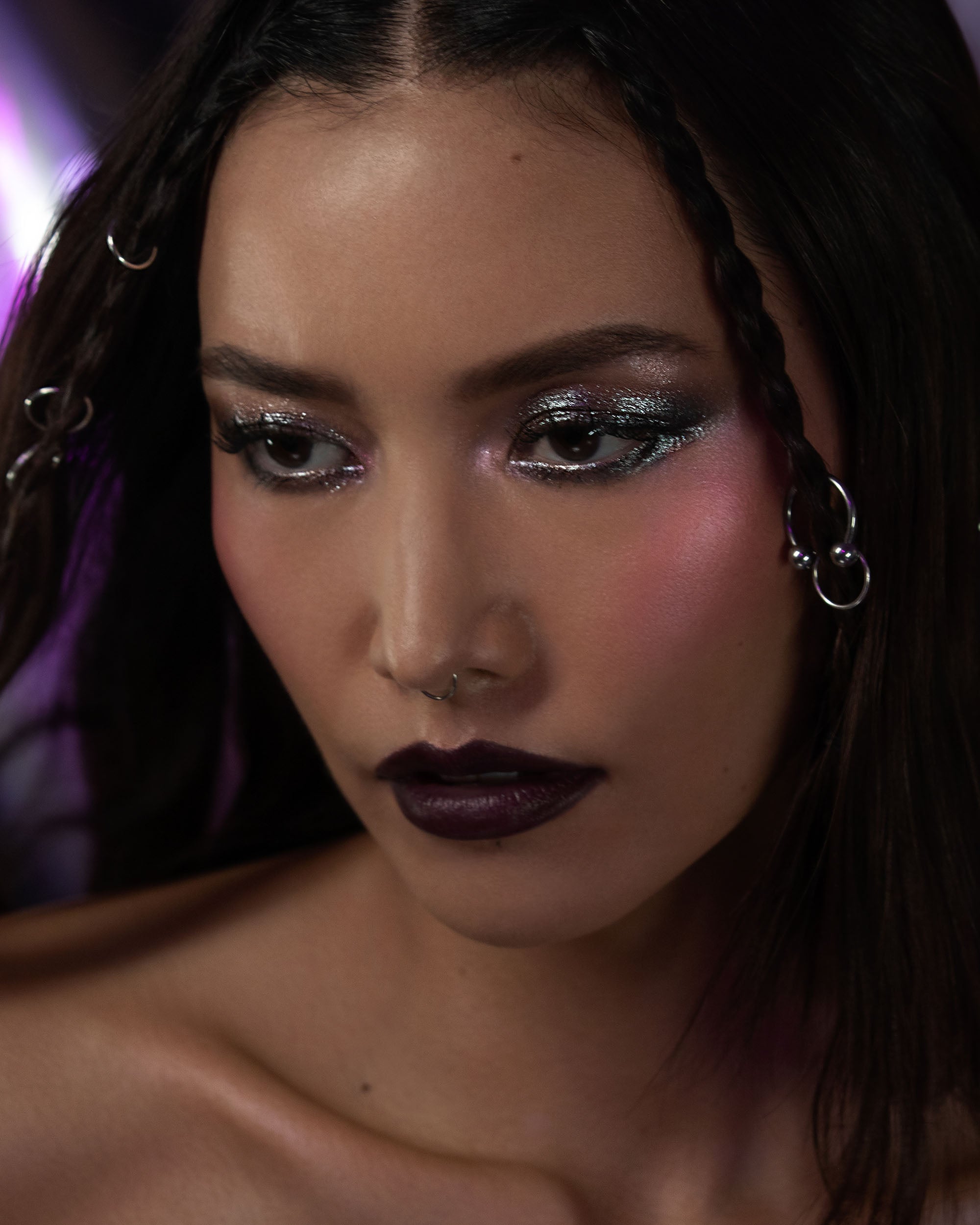 Close-up of a person with dark hair and dramatic makeup, wearing earrings.