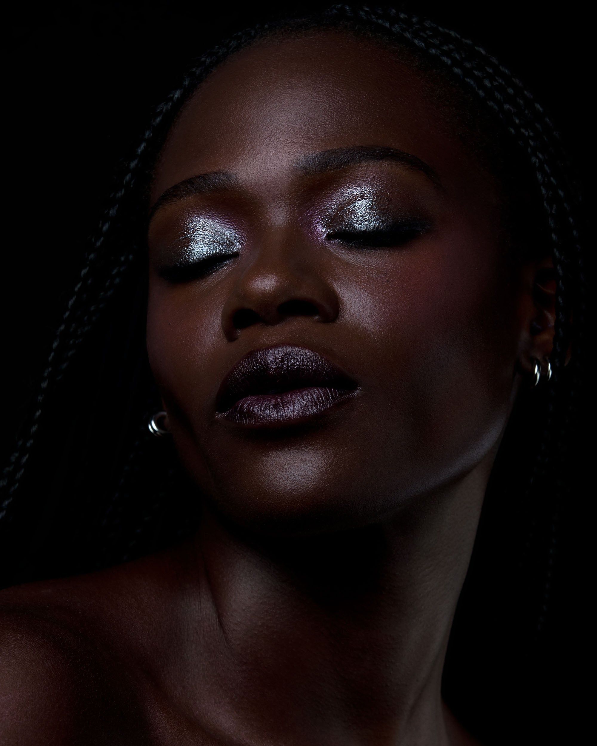 Close-up of a person with deep skin and metallic eye makeup against a dark background