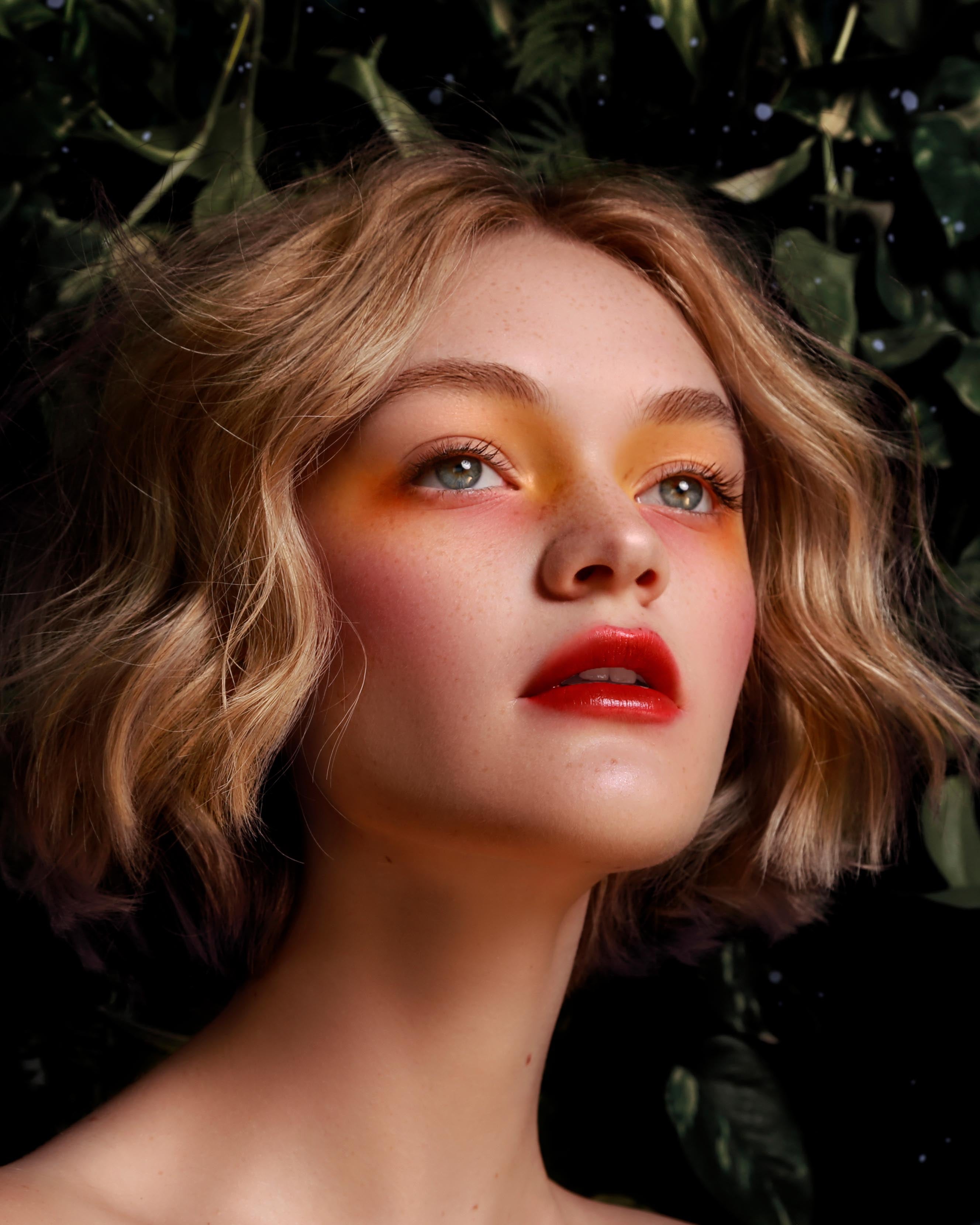 Close-up of a model with fair skin and pink, yellow, and red makeup against a dark leafy background
