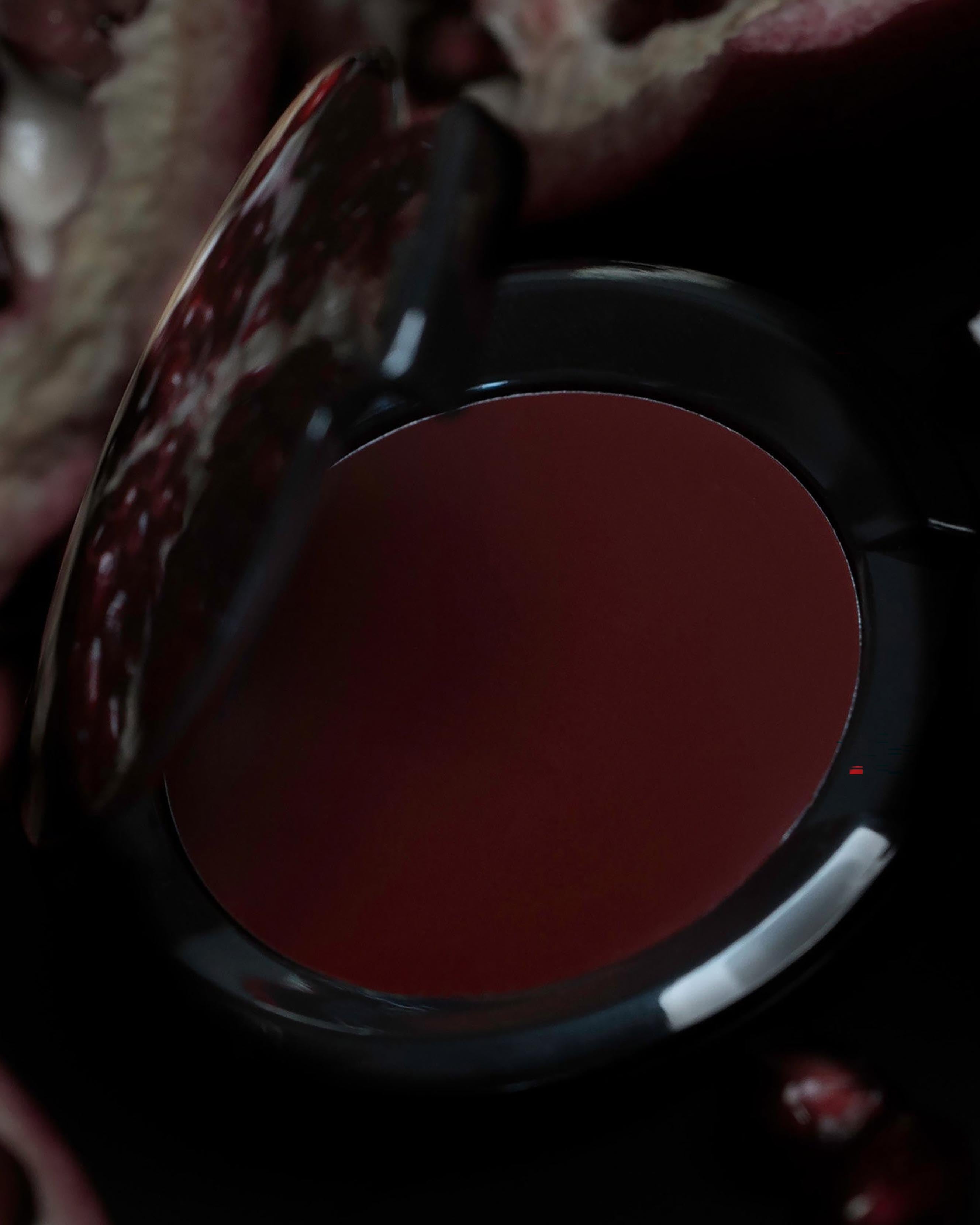Burgundy red makeup in black compact on a dark floral background
