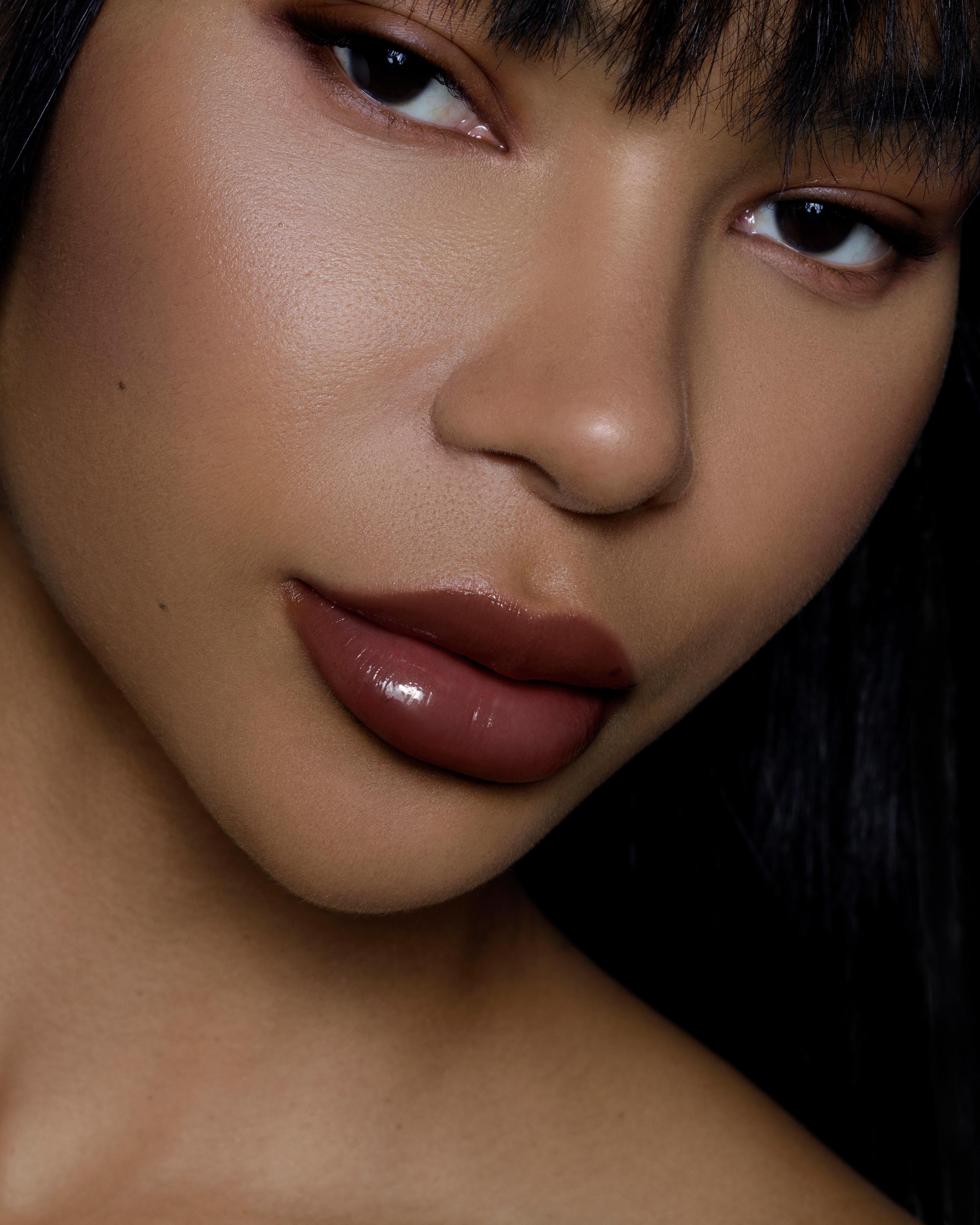 Close-up of a model with medium-deep skin wearing burgundy red makeup on lips, eyes, and cheeks