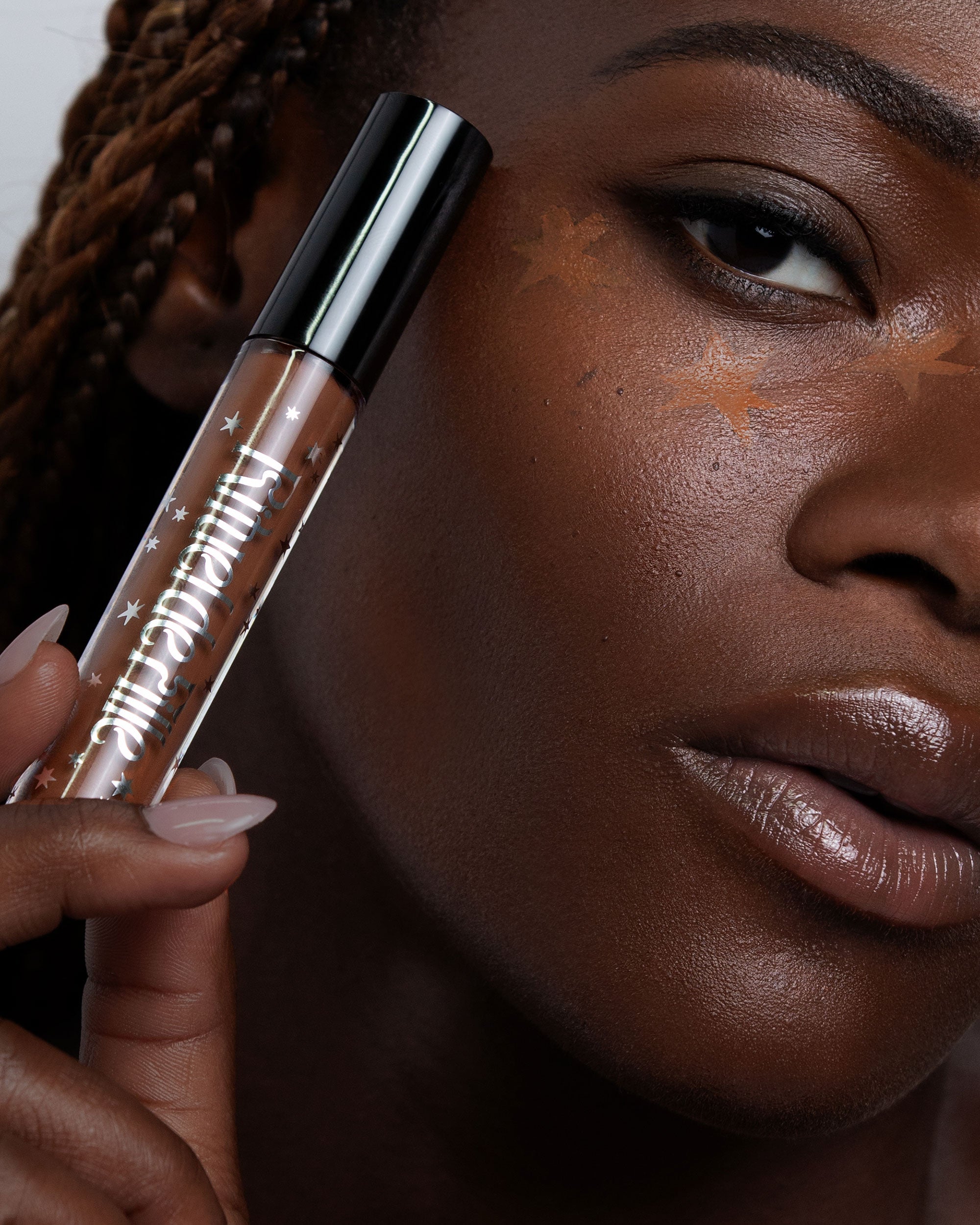 a person holding a closed vial of Rituel de Fille Soft Sorcery Weightless Serum Concealer in shade Spell 201 in front of their face, with three stars applied in concealer under the eye